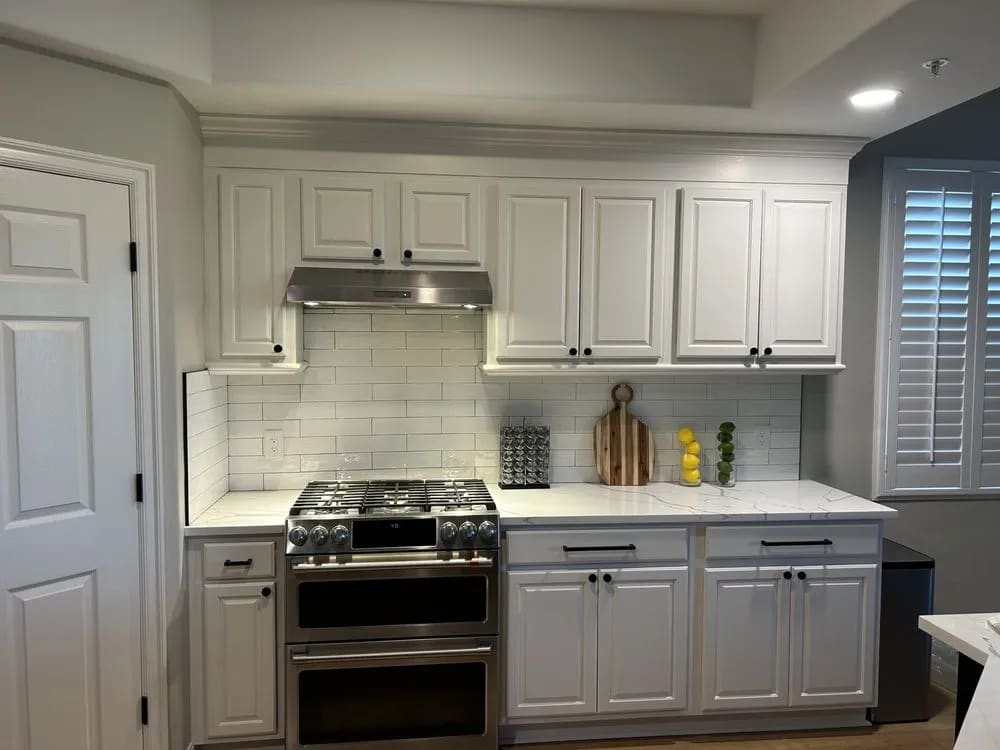 White kitchen with raised-panel cabinets, crown molding, subway tile backsplash, marble-look counters and a stainless double-oven range
