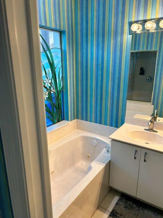 Bathroom before: striped wallpaper, a jetted tub and a small single vanity beside the stained-glass window
