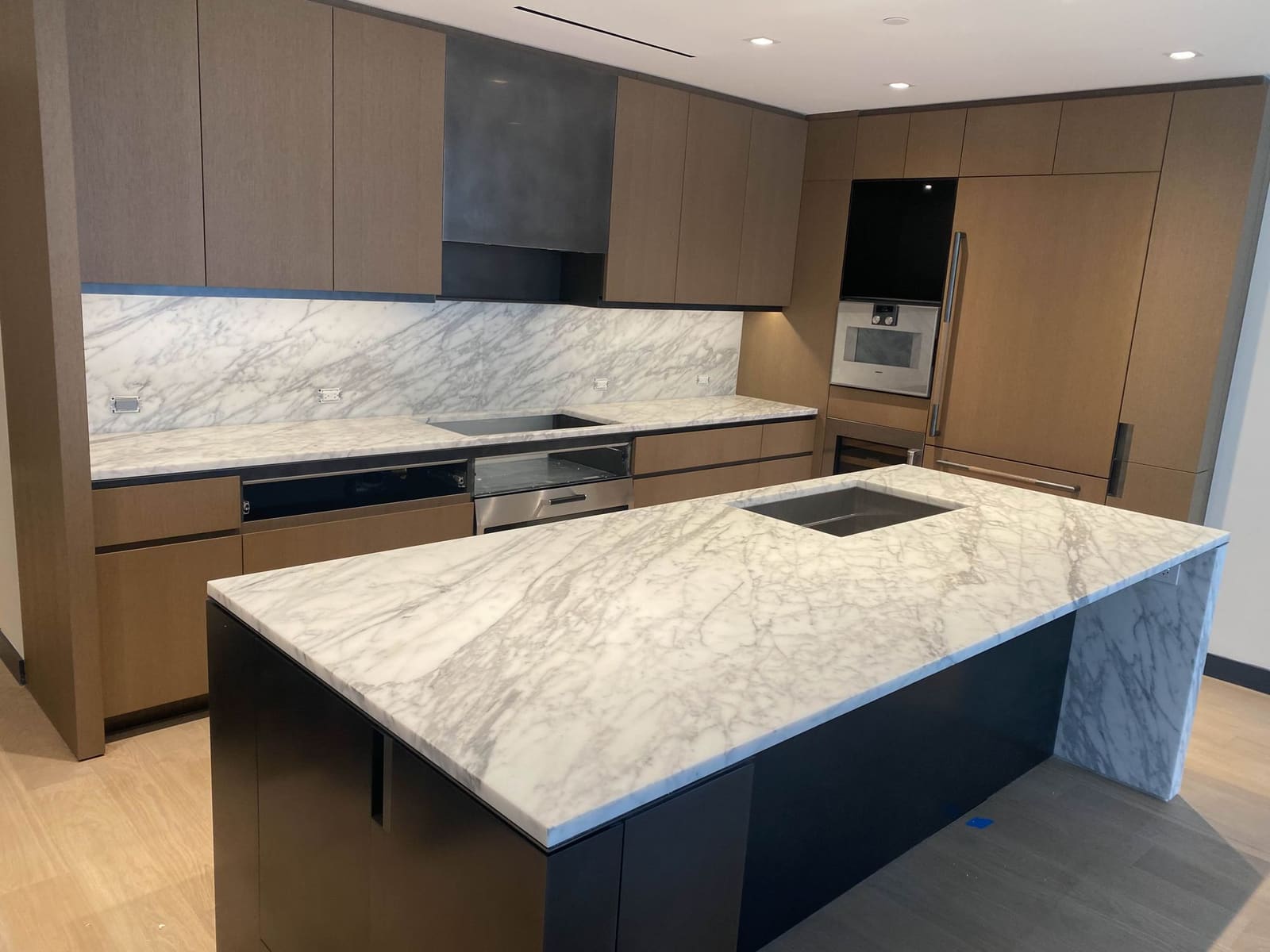 Modern kitchen with rift-cut oak flat-panel cabinetry, Calacatta marble backsplash and a waterfall marble island